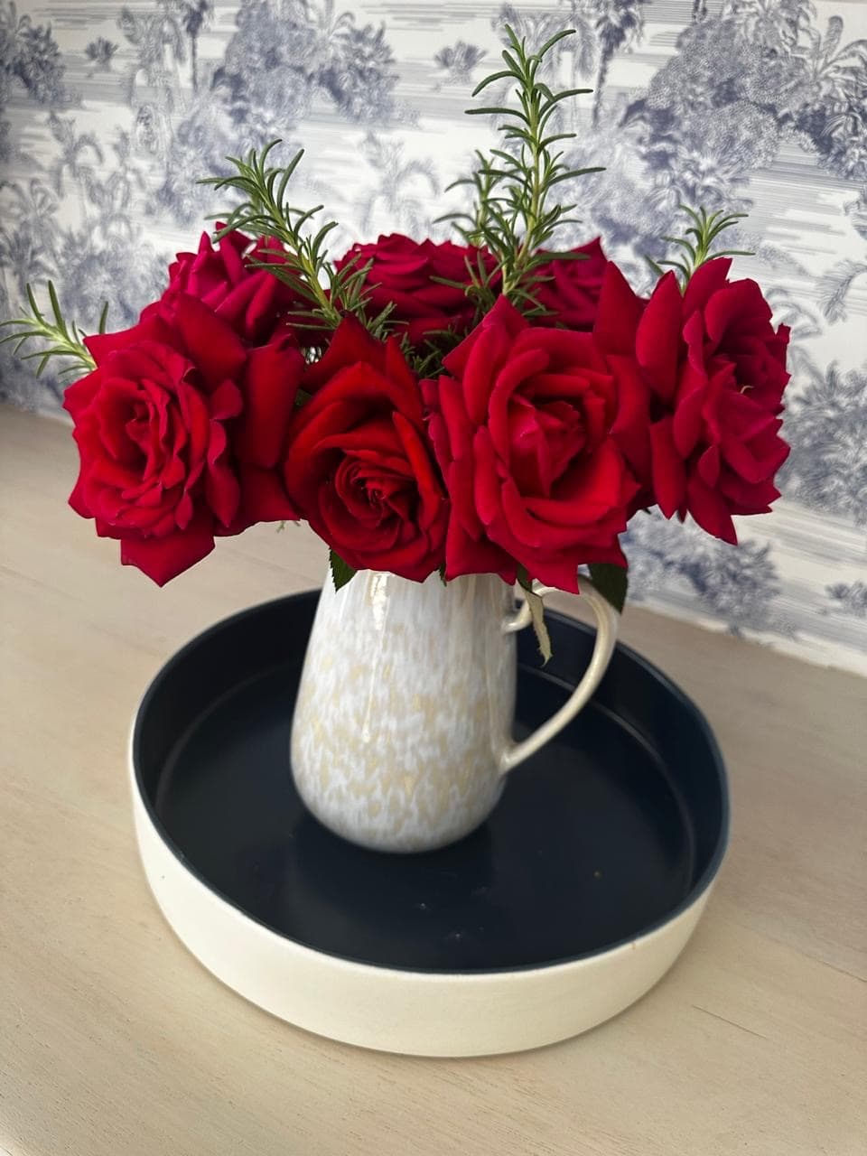 red roses in cream vase against a blue and white background